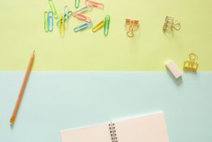 Top view of colorful stationery items, including a notebook, pencil, paperclips, and an eraser on pastel background.