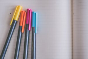 A collection of colorful pens resting on an open lined notebook, creating a vibrant and inviting workspace.